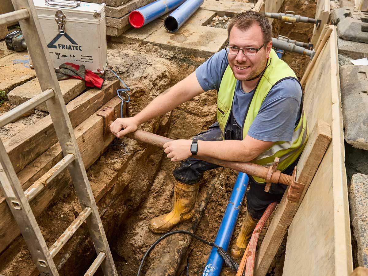 Fachkraft im verbauten Leitungsgraben mit neuen Versorgungsleitungen