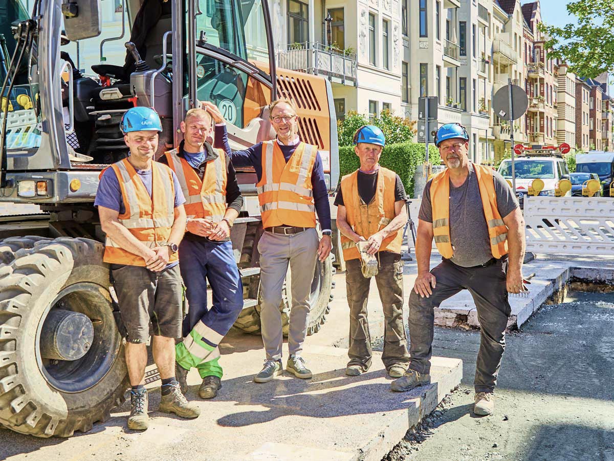 Kolonne und Bauleitung stehen gemeinsam vor dem Bagger auf einer Baustelle in der Stadt