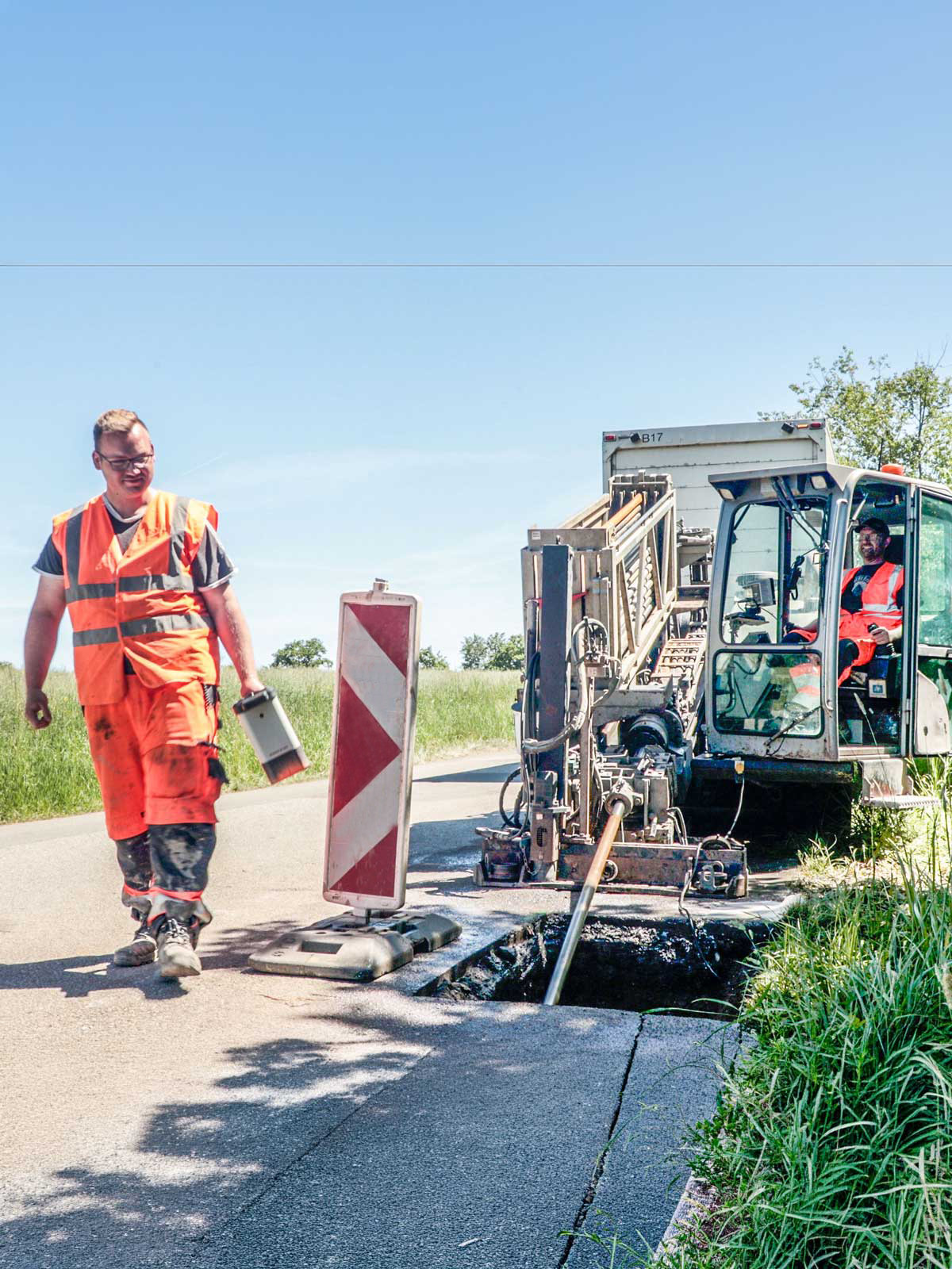 Horizontalbohranlage an einer Landstraße, im Vordergrund eine Fachkraft mit Ortungsgerät